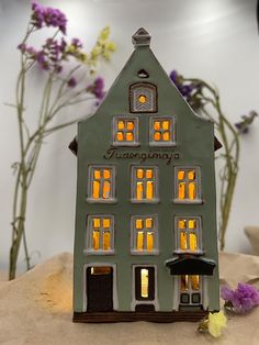 a small green house sitting on top of a table next to purple and yellow flowers