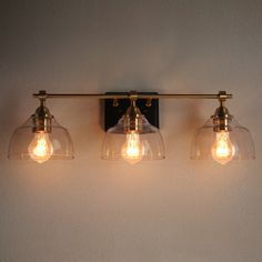 three light fixtures mounted on the wall with clear glass shades and brass fittings,