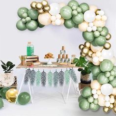 an arch made out of balloons and greenery sits in front of a party table