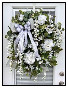 a wreath with white flowers and green leaves hangs on the front door, ready to be hung