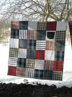 two quilts hanging on a clothes line in the snow, with trees and grass behind them