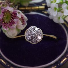 a diamond ring sitting on top of a purple plate next to flowers and a pen