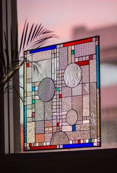 a stained glass window sitting on top of a window sill next to a potted plant