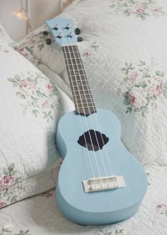 a blue ukulele sitting on top of a bed next to a white pillow