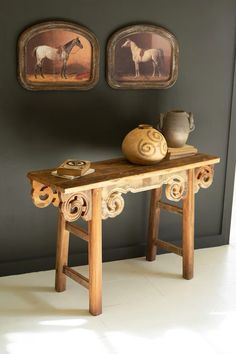 a wooden table with vases on it in front of two framed pictures and paintings