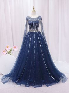 Aeonian elegance embodied in a dress, this blue gown is truly breathtaking! Capturing the essence of celestial beauty, it boasts an intricate overlay of sparkling sequins and delicate beading that illuminates the deep blue fabric beneath. The gown's fitted bodice highlights a sophisticated silhouette, cinched at the waist with a band of embellishments that enhance its figure-flattering design. Long, sheer sleeves and a gently scooped neckline add a touch of royal grace, perfect for a prom queen. The expansive skirt, speckled with glimmers like distant stars, flows into a soft, sweeping hem, making every movement a statement of grace and poise. This dress is designed for those who dream of a magical evening, wrapped in glamour and inspired by the night sky. Dark Blue Fantasy Gown, Starfall Ball Gown, Sapphire Ball Gown, Dark Blue Fantasy Dress, Royal Blue Gowns Elegant, Royal Blue And Gold Dress, Galaxy Wedding Dress, Blue Fantasy Dress, Blue Medieval Dress