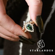 a woman's hand holding a ring with green and white stones on it, in front of a black background