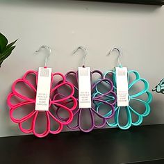 three pairs of scissors hang from hooks on a wall next to a potted plant