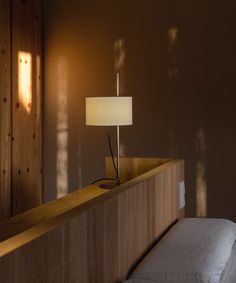 a bed with a lamp on top of it next to a wooden headboard and wall