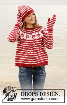 a woman wearing a red and white knitted sweater standing in front of the water