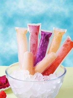 four different colored candles in a bowl with ice and raspberries on the side