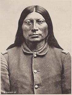 an old black and white photo of a native american man with long hair, wearing a uniform