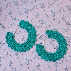 a pair of green crocheted hoop earrings sitting on top of a pink surface