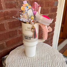 a cup filled with lots of different things on top of a white table next to a brick wall