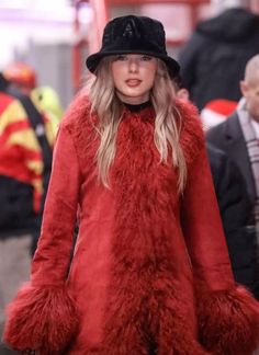 a woman in a red coat and black hat walking down the street with other people behind her