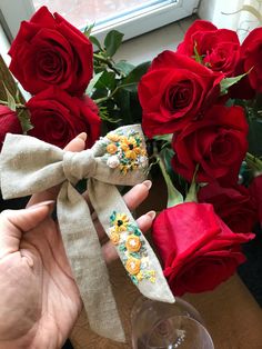 a person is holding a bow tie with roses in the background and a glass of wine