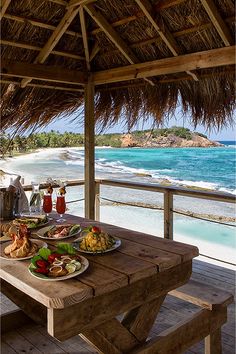 a wooden table with plates of food on it near the ocean and beach in the background