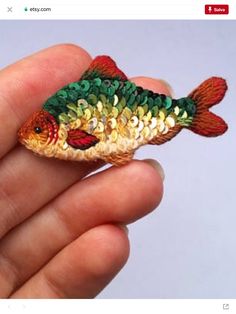 a hand holding a small toy fish in it's left hand, with the word sequins on its body