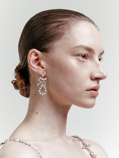 a woman in a white dress is wearing large silver earrings with flowers on the side