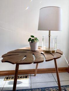 a wooden table with a plant on it and a lamp next to it in front of a white wall