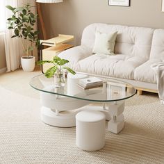 a living room with a white couch and glass table in the middle, surrounded by potted plants