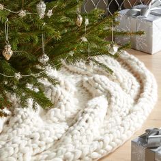 a white knitted blanket under a christmas tree with presents on the floor next to it