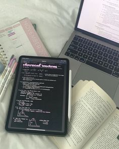 an open laptop computer sitting on top of a bed next to notebooks and books