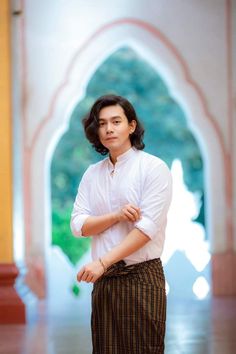 a man standing with his arms crossed in front of an archway and wearing a white shirt