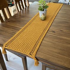 a crocheted table runner sits on top of a dining room table with a potted plant