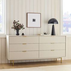 a white dresser with two vases and a black lamp on it in front of a window