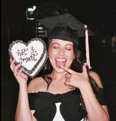 a woman in graduation cap and gown holding a heart shaped cake with writing on it