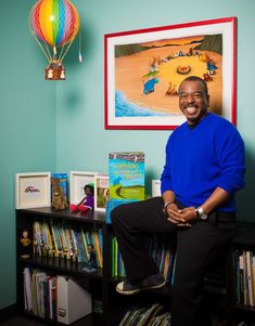 a man sitting on top of a book shelf in front of a wall with books