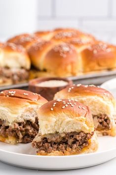 two hamburger sliders cut in half on a plate next to a tray of rolls