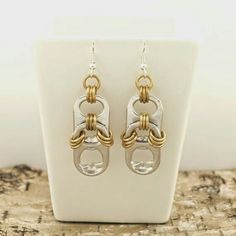 a pair of gold and silver earrings sitting on top of a white stand