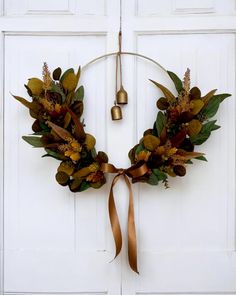 a wreath is hanging on the front door with a bell in the middle and leaves around it