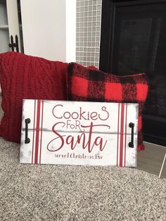 a wooden sign that says cookies for santa on it next to some red and white pillows