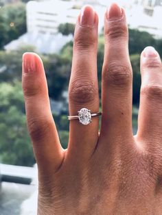 a person's hand with a diamond ring on top of their finger and trees in the background