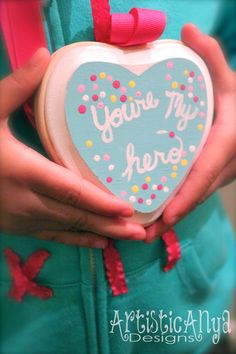 a person holding a heart shaped cookie with the words you're my hero written on it