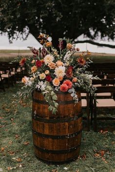 a wooden barrel with flowers and greenery on the ground next to rows of chairs