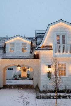 a white house with christmas lights on it's windows and snow falling from the roof