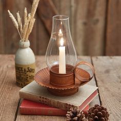 a candle that is sitting on top of some books next to a vase and pine cones