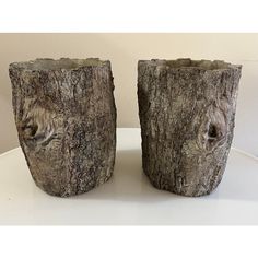 two vases made out of tree trunks sitting on a white table with a wall in the background