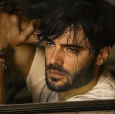 a man with long hair and beard sitting in a car looking out the window at something