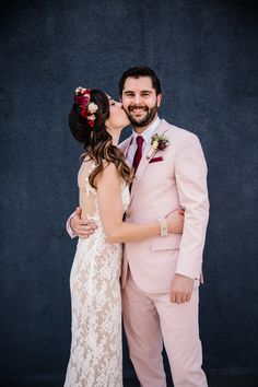 a bride and groom kissing each other in front of a black wall at their wedding