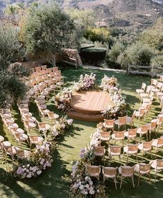 an outdoor ceremony setup with wooden chairs and flowers on the ground, surrounded by greenery