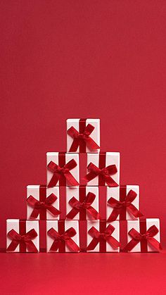 a stack of white gift boxes with red bows on them, sitting in front of a red background