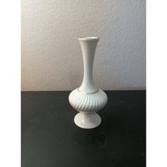 a white vase sitting on top of a black table next to a wall and floor