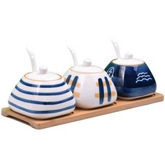 three ceramic teapots sitting on a wooden tray with white and blue striped lids