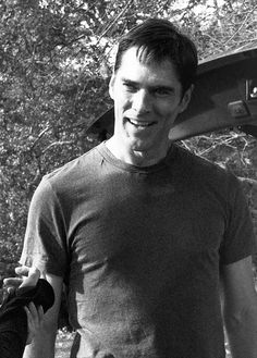 black and white photograph of a man holding a skateboard in his hand while standing next to trees