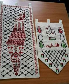 two pieces of cross - stitched cloth with designs on them sitting on a table